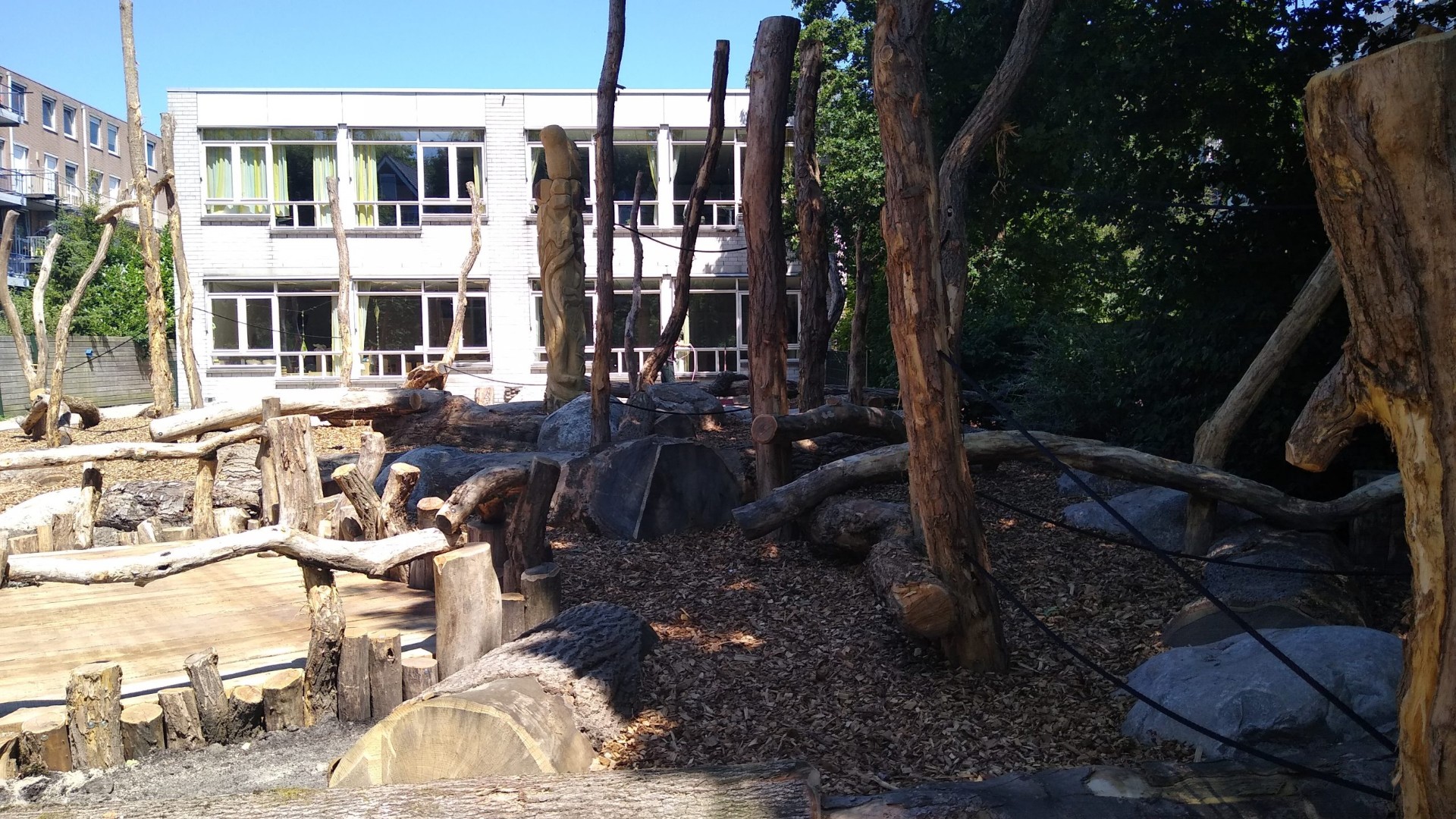 Natuurlijk speelbos met boomstammen, palen en keien op schoolplein