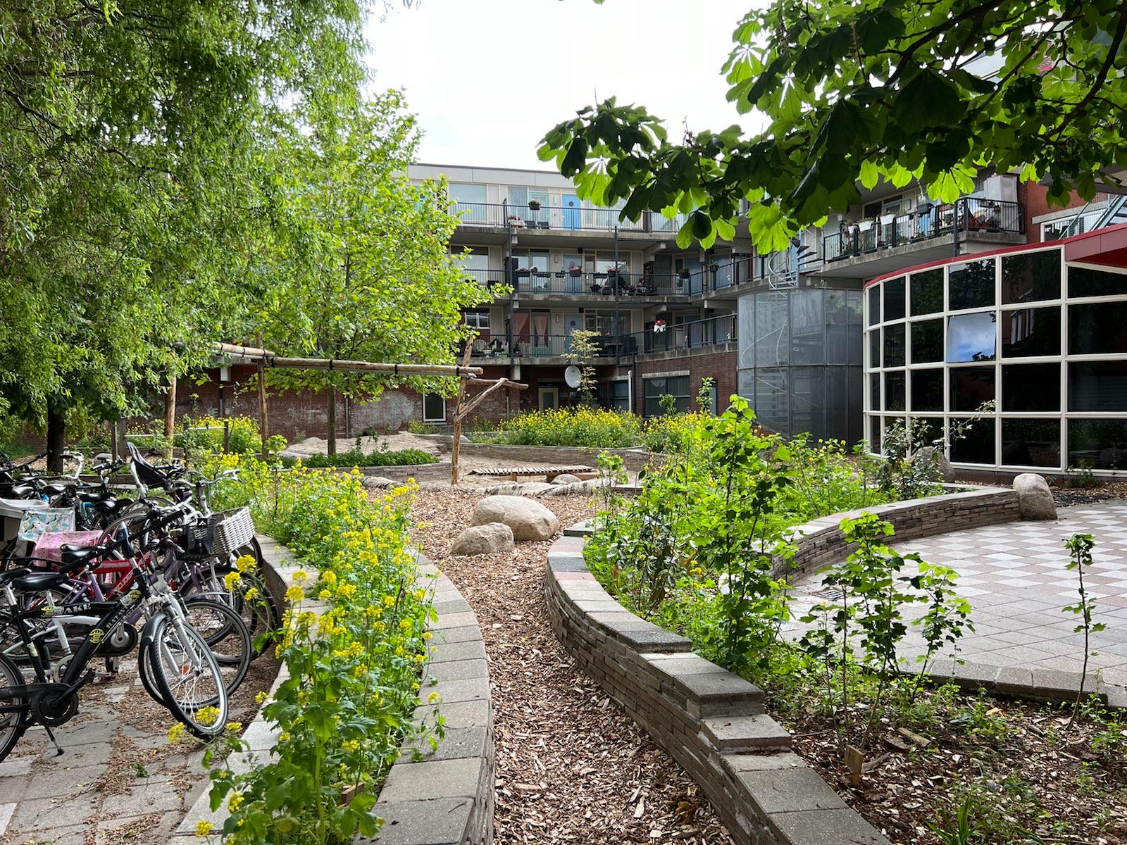 Groene binnentuin met bloemen, struiken en speelplekken tussen flats