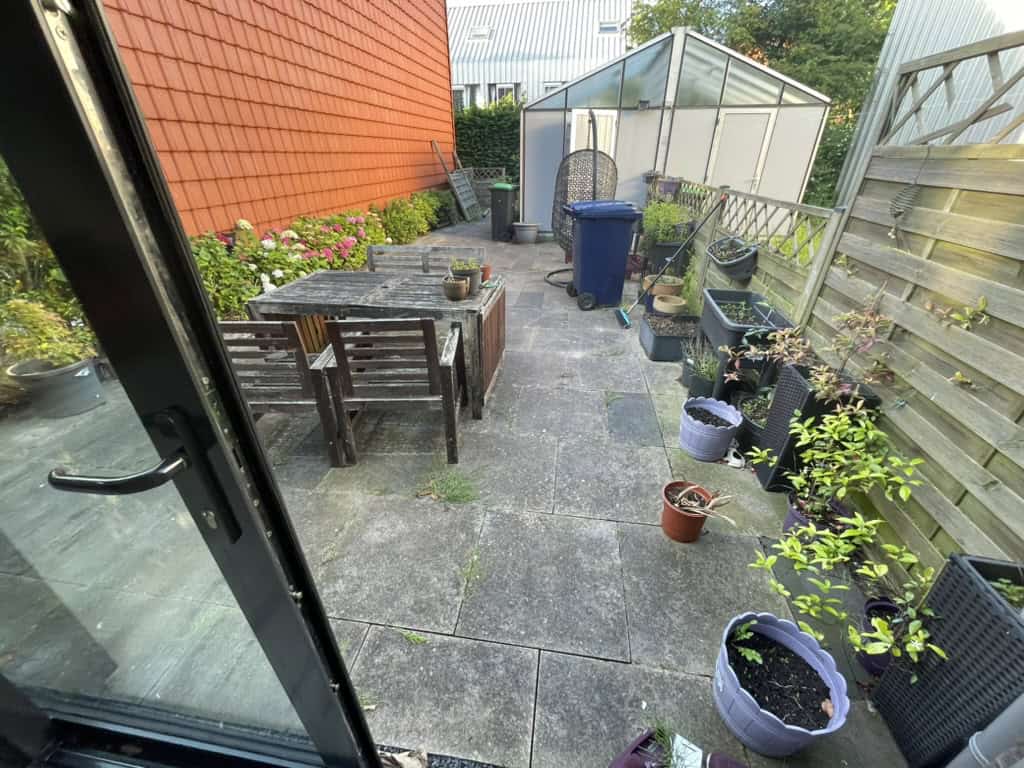 De tuin voor de verbouwing met betegeld terras en plantenbakken